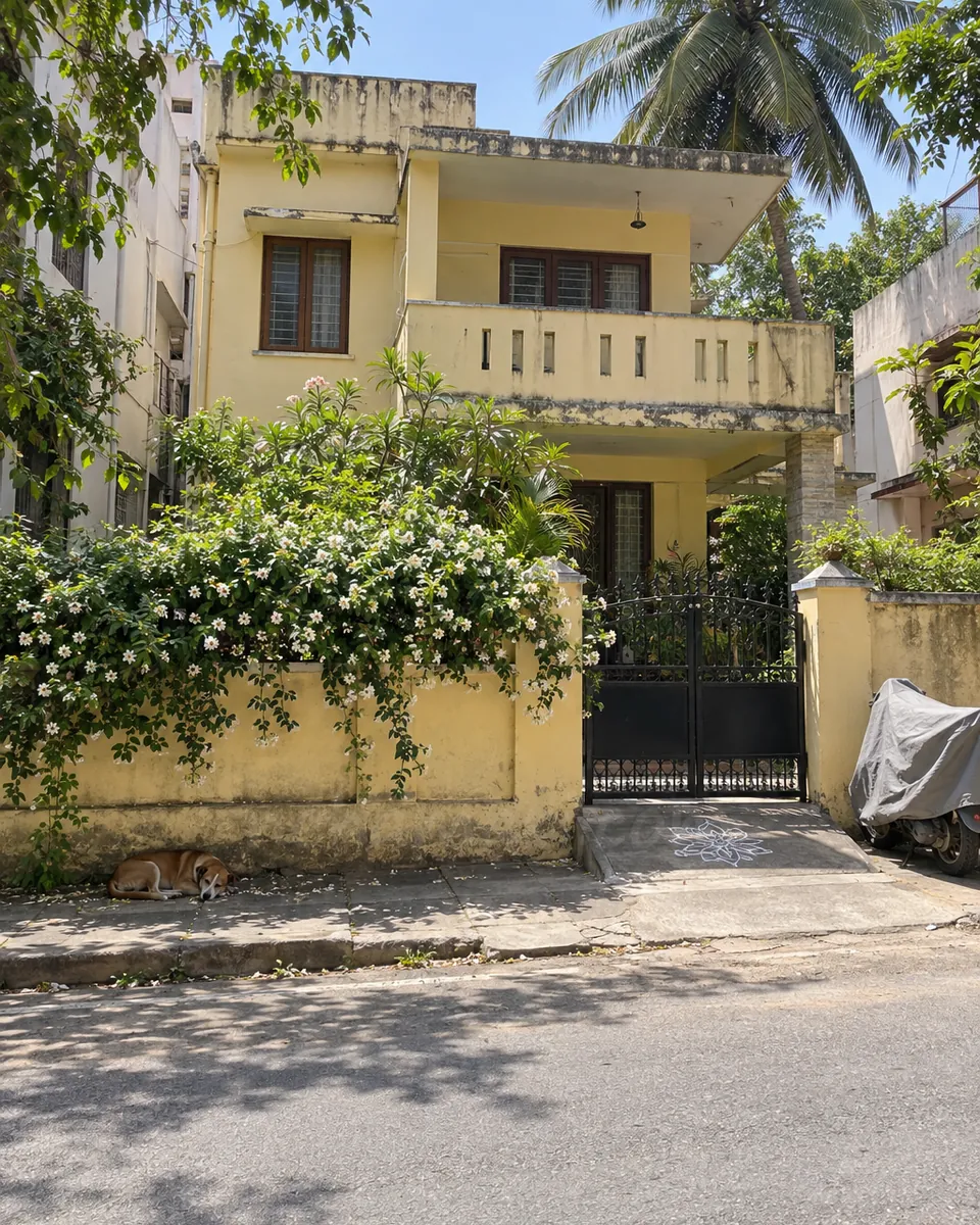 A quiet Jayanagar street at midday, an old house with jasmine on the compound wall and a closed iron gate