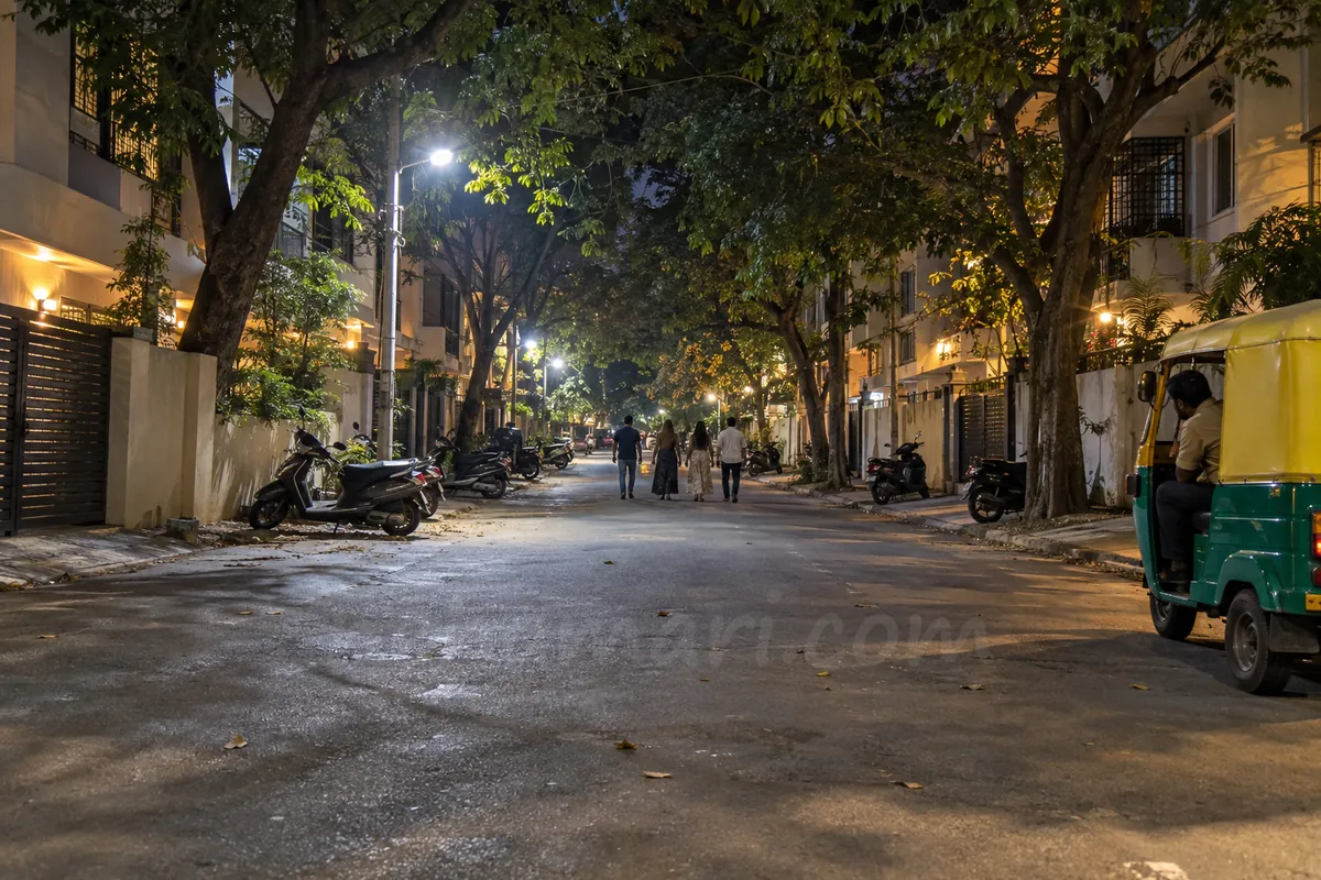 A quiet tree-lined inner road in Koramangala at night, scooters parked on both sides and an auto waiting at the kerb