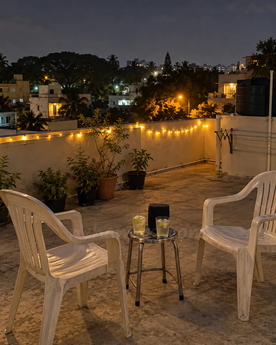 Two plastic chairs, a small speaker and fairy lights on a quiet Sanjay Nagar rooftop at night, set for music