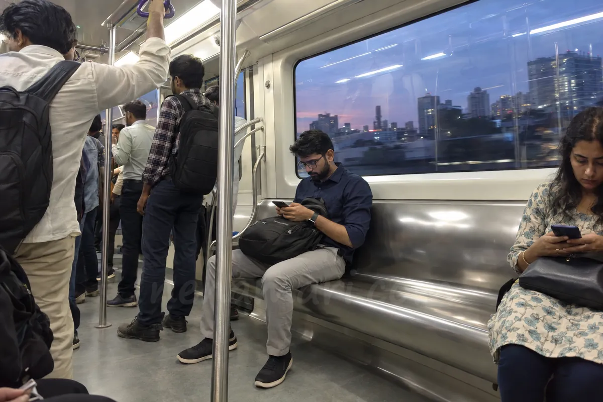 A man on a Namma Metro train scrolls a busy group chat on his phone on the way home